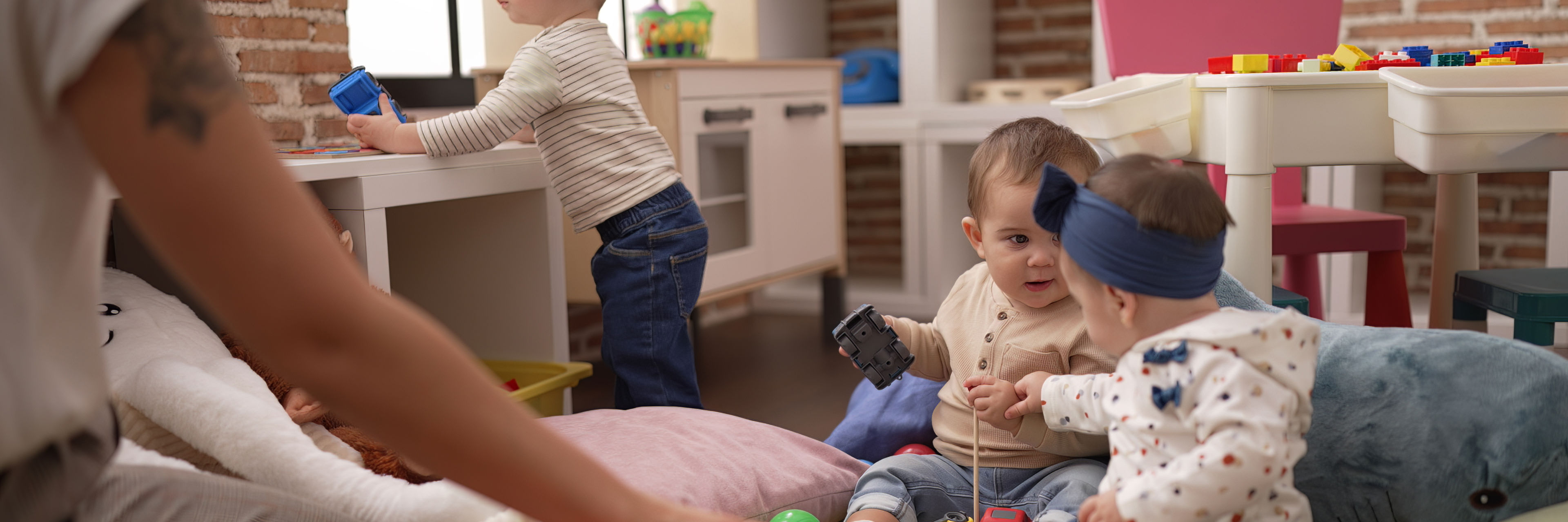 To blebørn leger på gulvet mellem små bolde - et lidt større barn står op og der sidder en voksen overfor dem