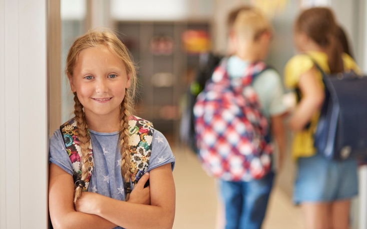 Pige med skoletaske kigger ind i kameraet. I baggrund ses tre kammerater.