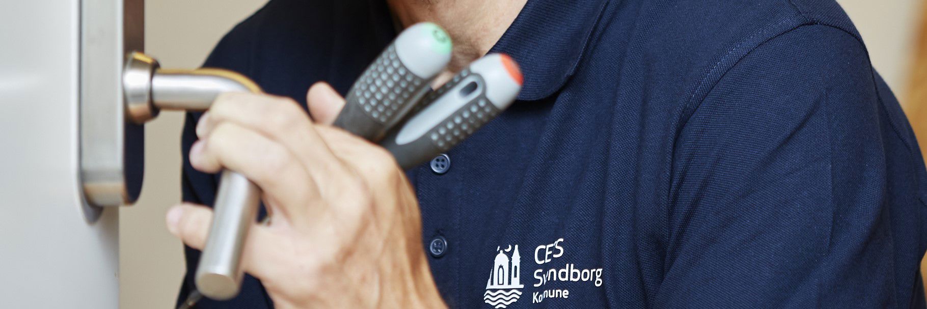 Hænder med værktøj som holder om et dørhåndtag.