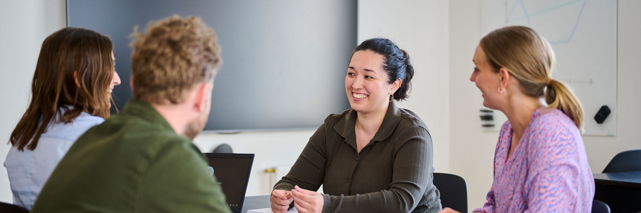 Tre kvinder og en mand sidder rundt om bord og snakker