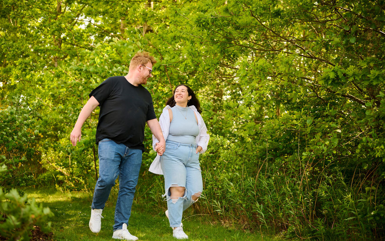 Mand og kvinde går med hinanden i hånden i grønne omgivelser