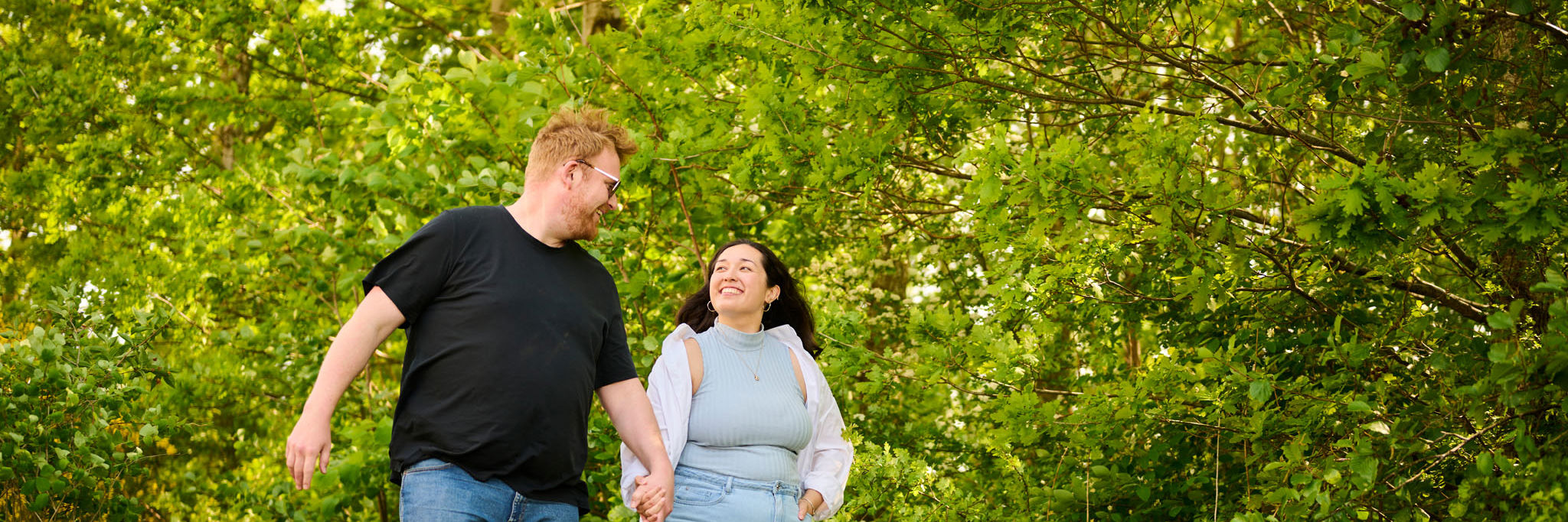 Mand og kvinde går med hinanden i hånden i grønne omgivelser