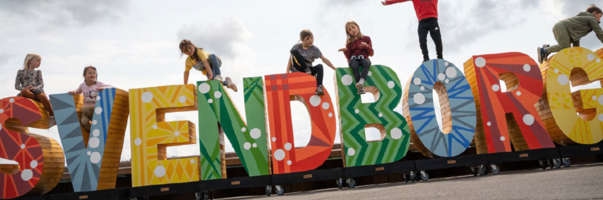 Børn fra indskolingen leger på store farverige bogstaver, hvor der står Svendborg