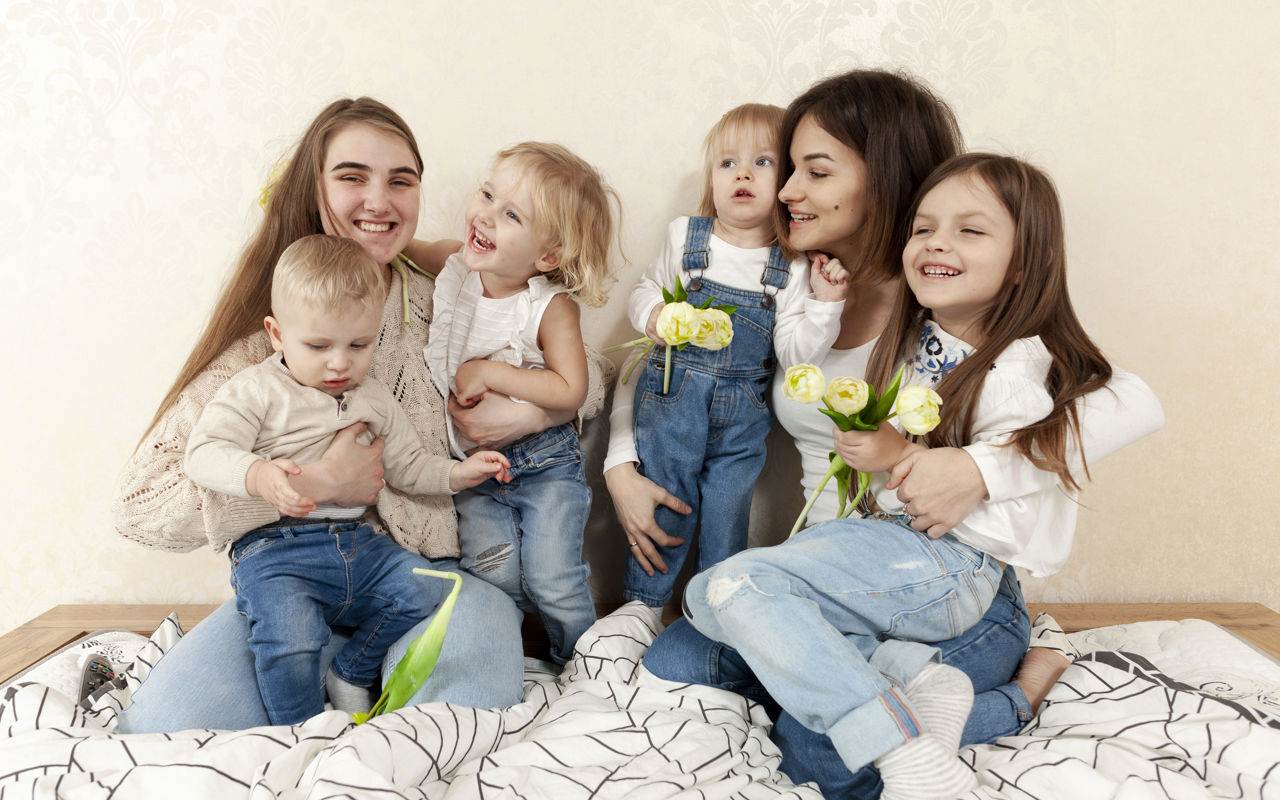 To kvinder og 4 børn sidder sammen i en seng