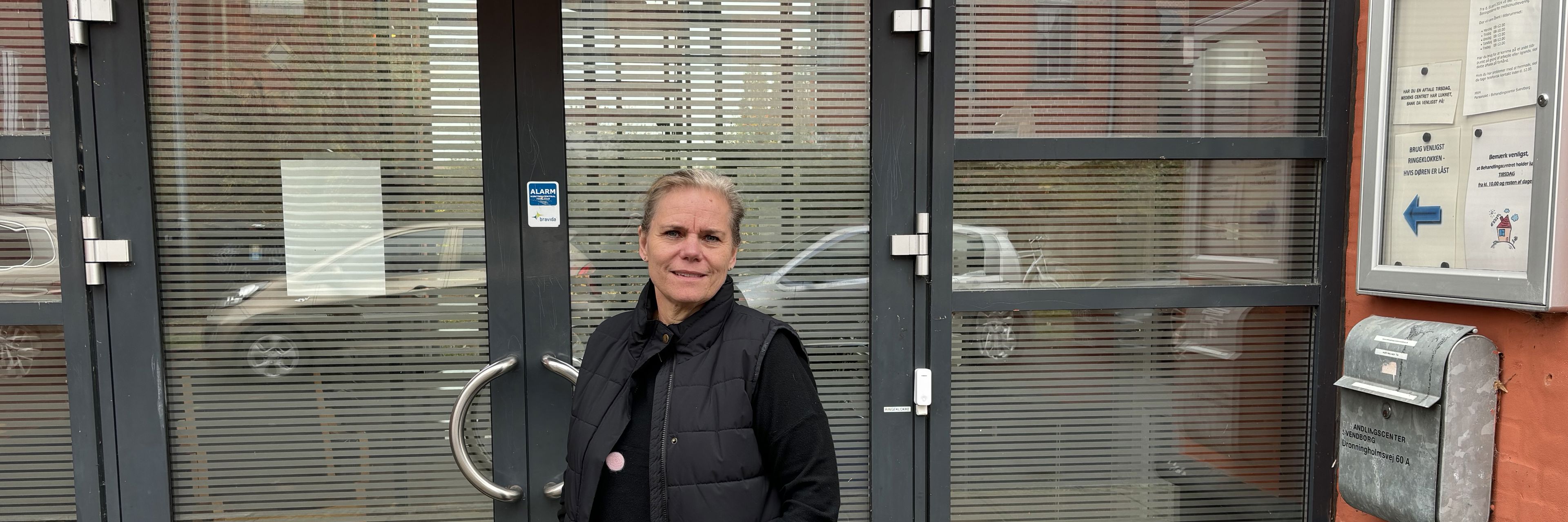 Kvinde i mørt tøj står foran en indgangsdør