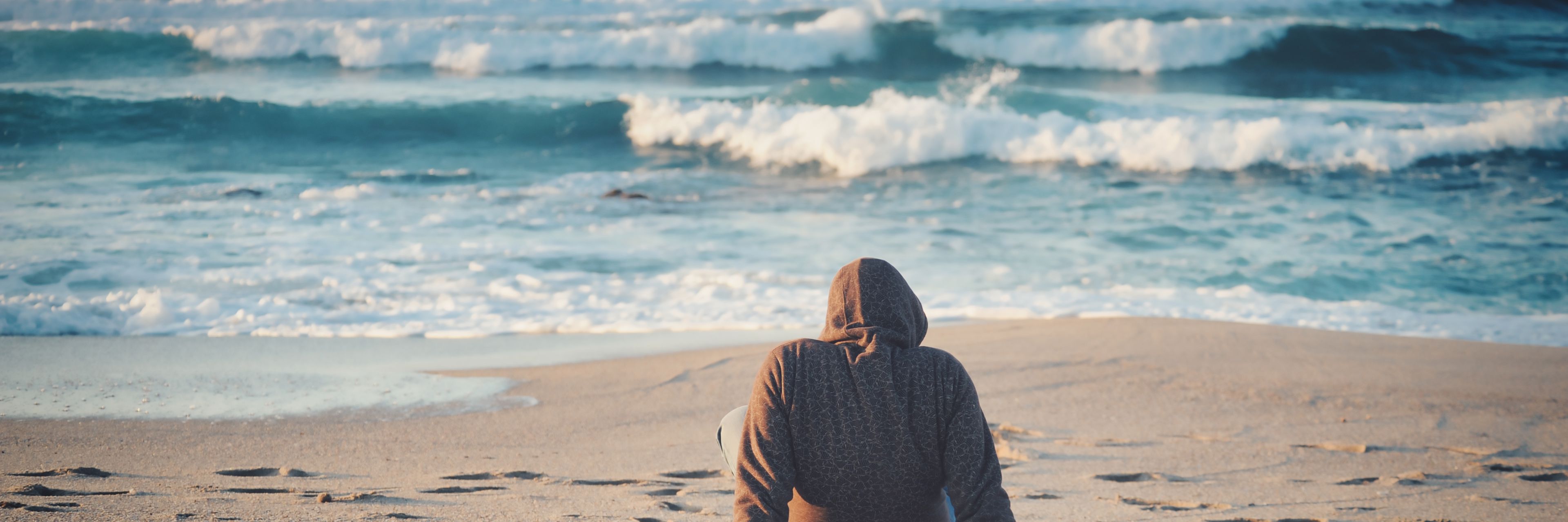 Person, der sidder med ryggen til og kigger på havets bølger