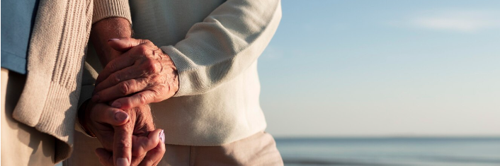 Ældre par hænder i hånden med havet i baggrunden