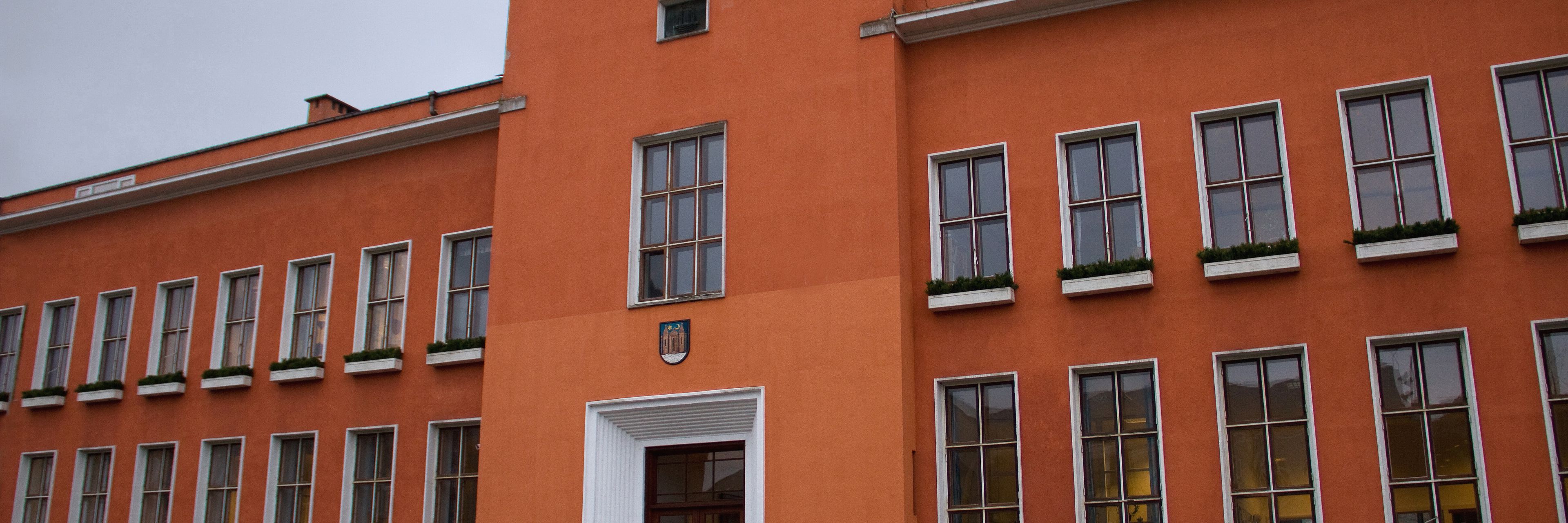 En stor rødlig bygning med brune og hvide vinduesrammer, der viser at bygningen har to etager.