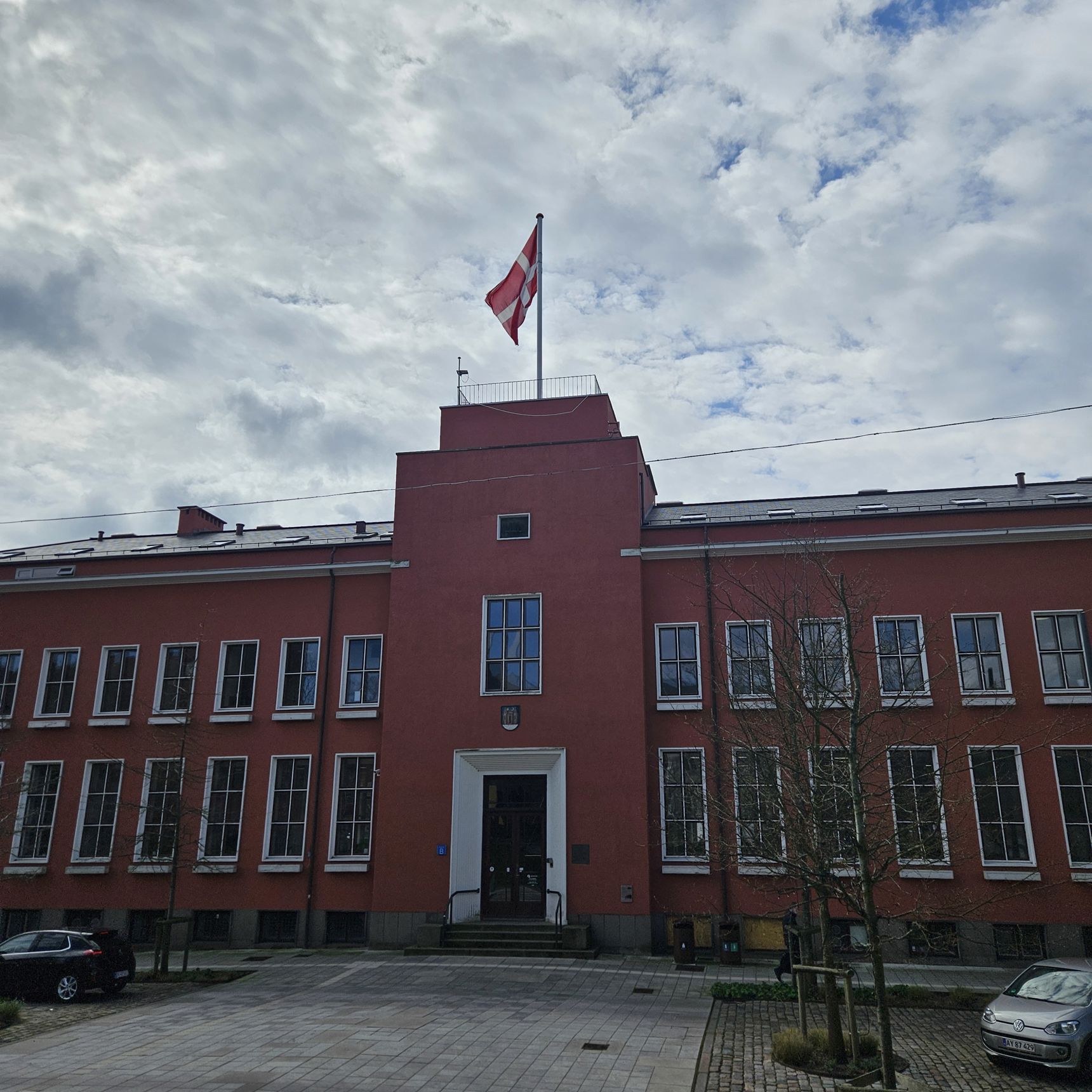 En to-etagers rødlig bygning med hvide vinduesrammer. Øverst på bygningen vejrer Dannebrog. Det er Svendborg Rådhus.