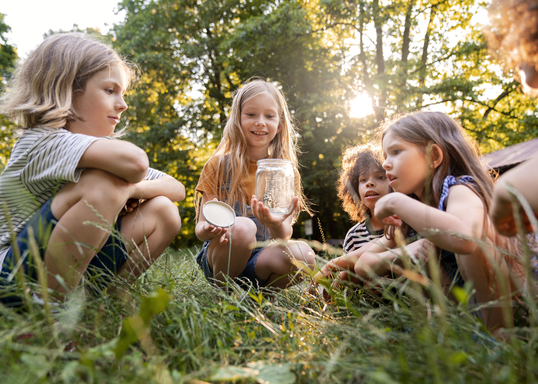 4 børn i rundkreds med sommerfugl i glas