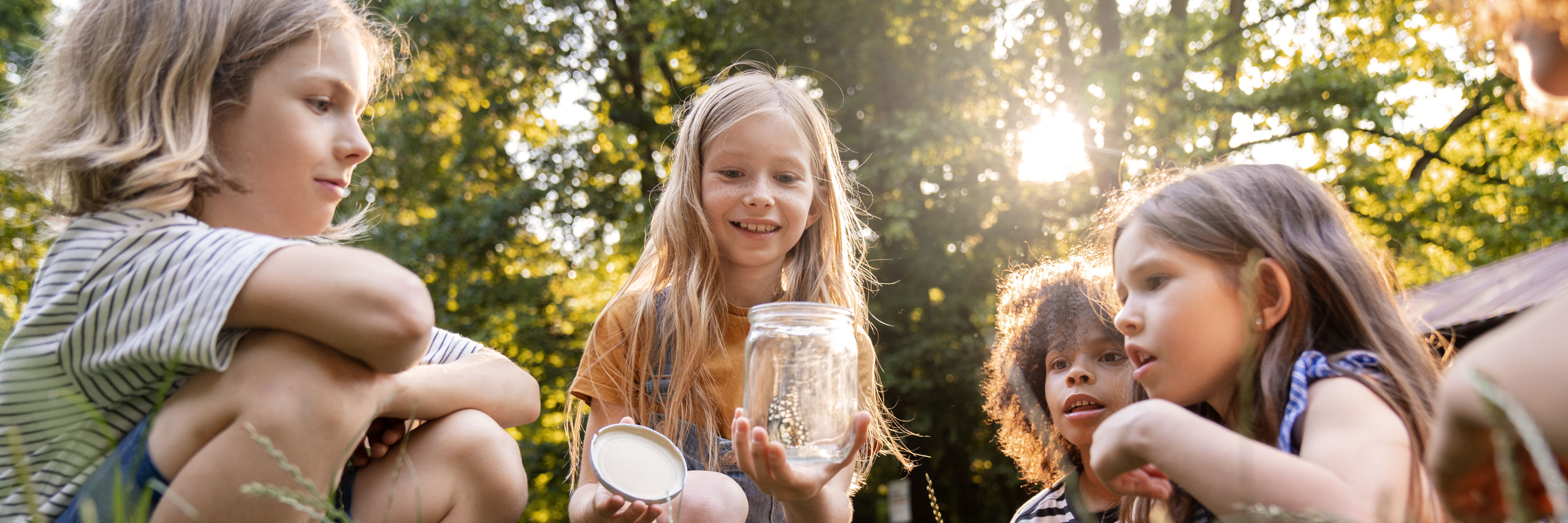 4 børn i rundkreds med sommerfugl i glas